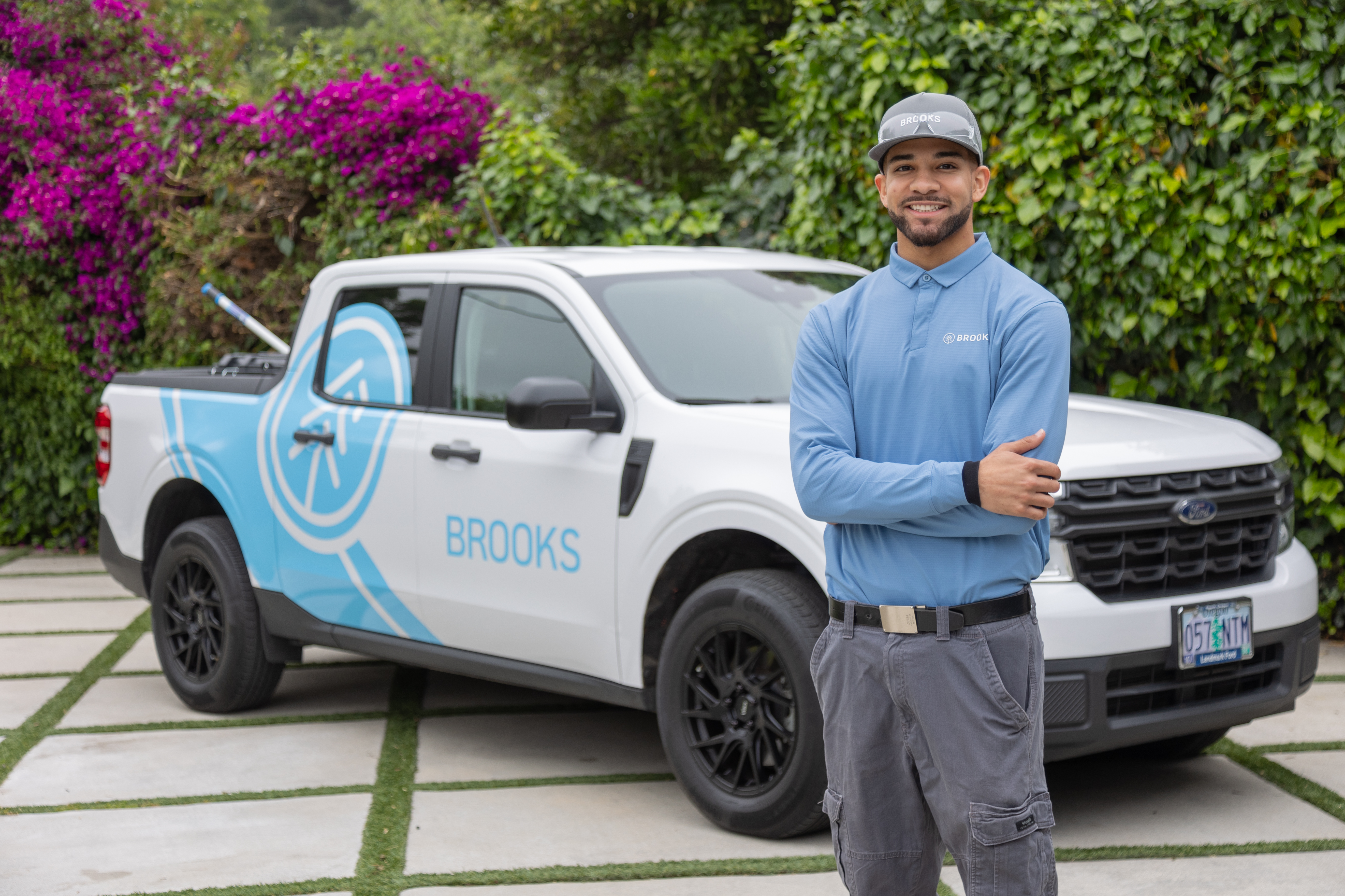 Brooks Pest Control technician in front of branded truck in Southern California driveway with flowering plants