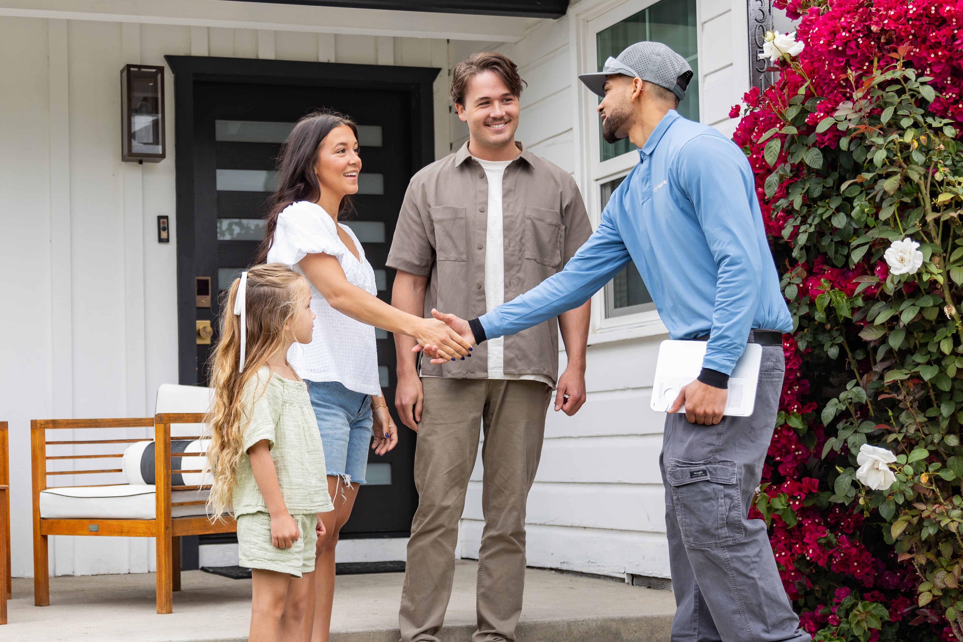 Brooks Pest Control technician greeted by family at front door of suburban home